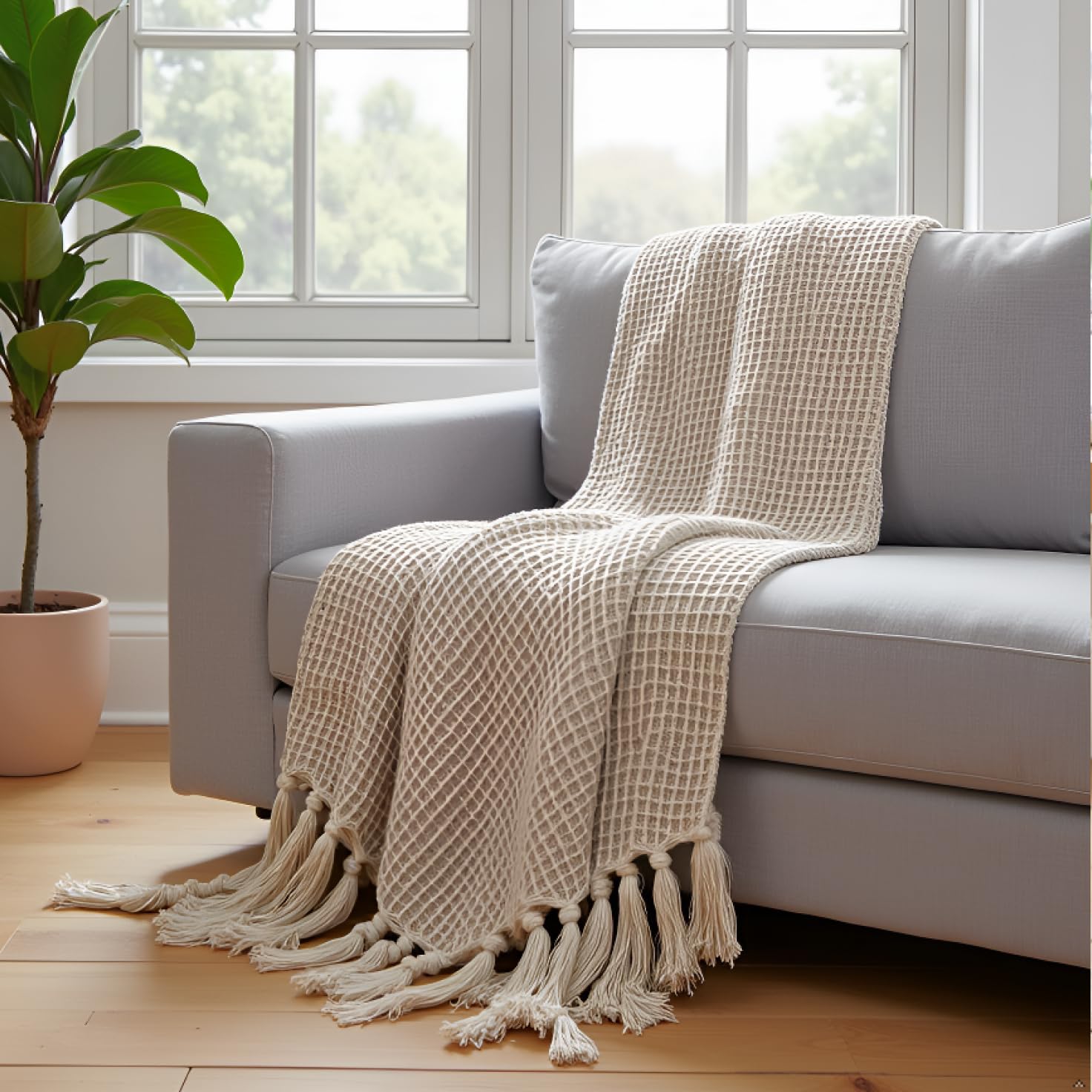 Beige checkered throw blanket with tassels draped over a gray sofa in a bright room with a plant.