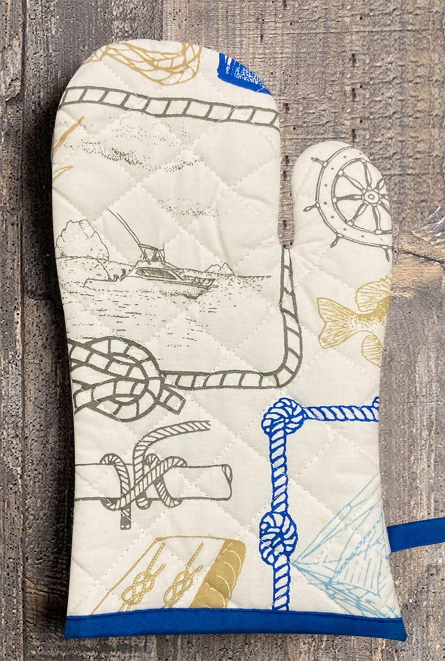 A pair of white and blue oven gloves with a nautical pattern, including a boat and ropes, laid out on a wooden surface.