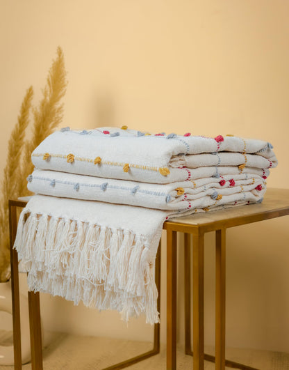 Stack of folded blankets with decorative patterns on a wooden table against a beige wall.