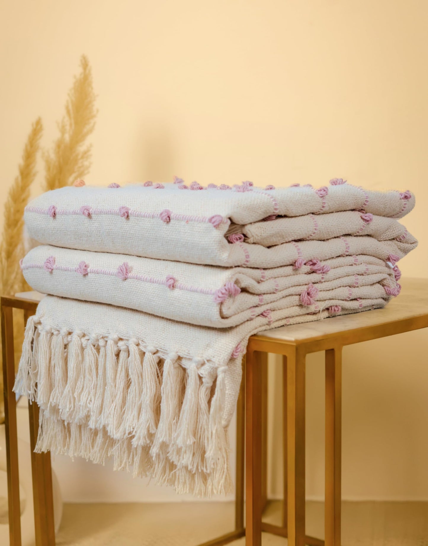 Stack of folded towels with tassels on a wooden table against a beige background