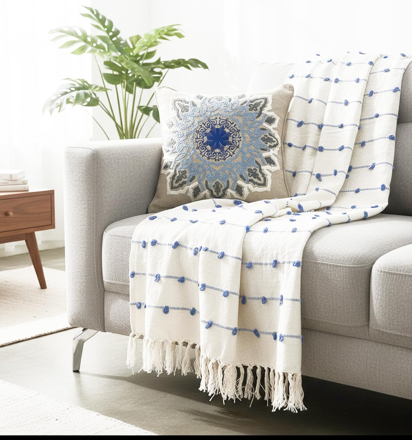 Gray sofa with a decorative pillow and white blanket with blue patterns in a living room setting.